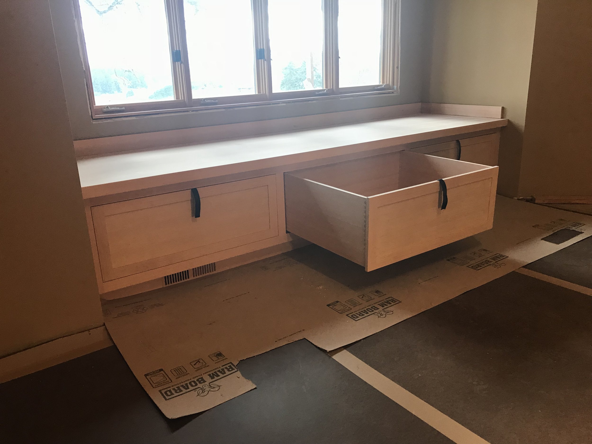 Ark Built Carpentry custom designed wooden built-in cabinet under the window, drawer open.