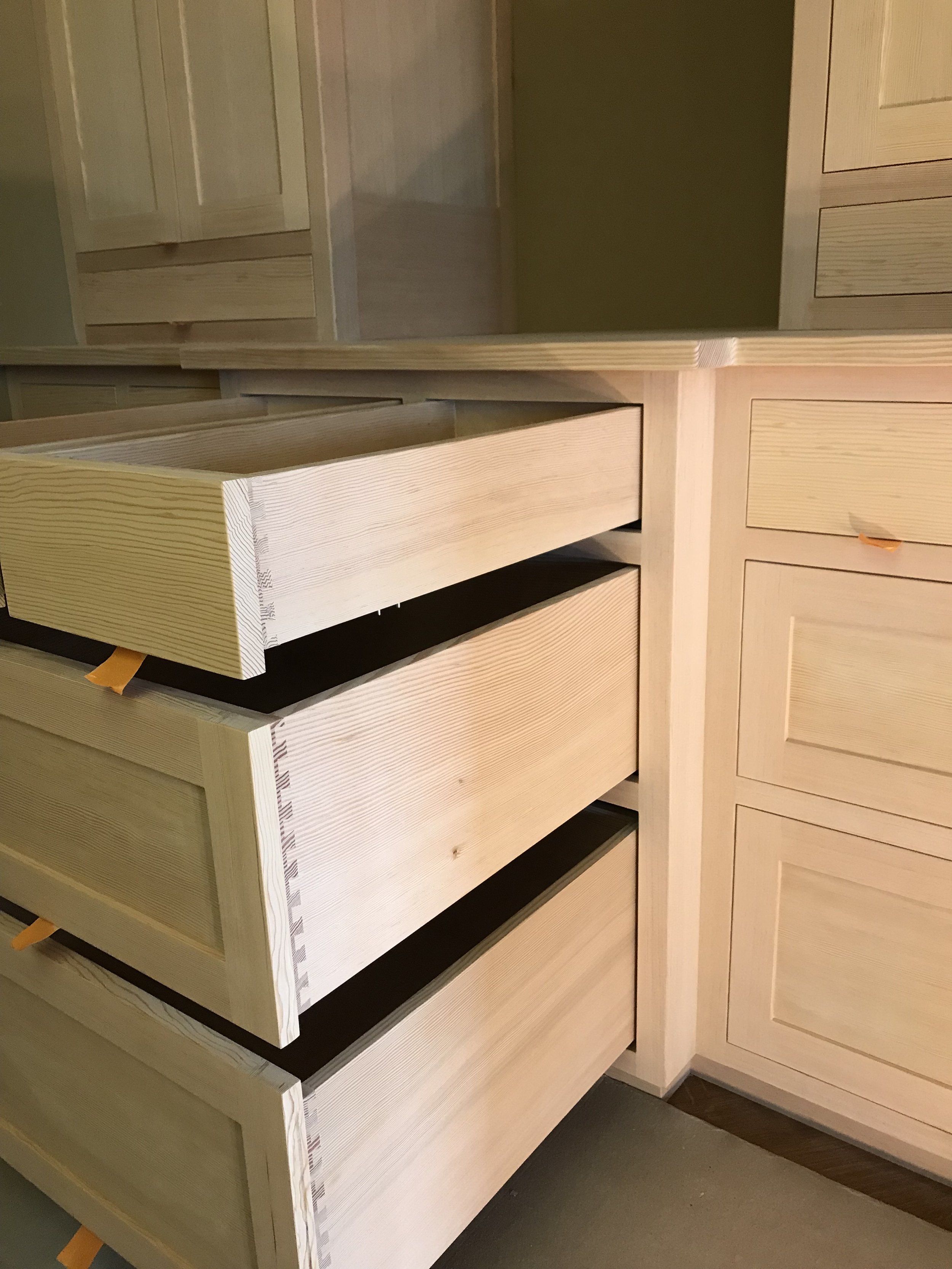 Ark Built Carpentry custom designed handcrafted wooden closet with multiple drawers and open compartments set against a green wall.