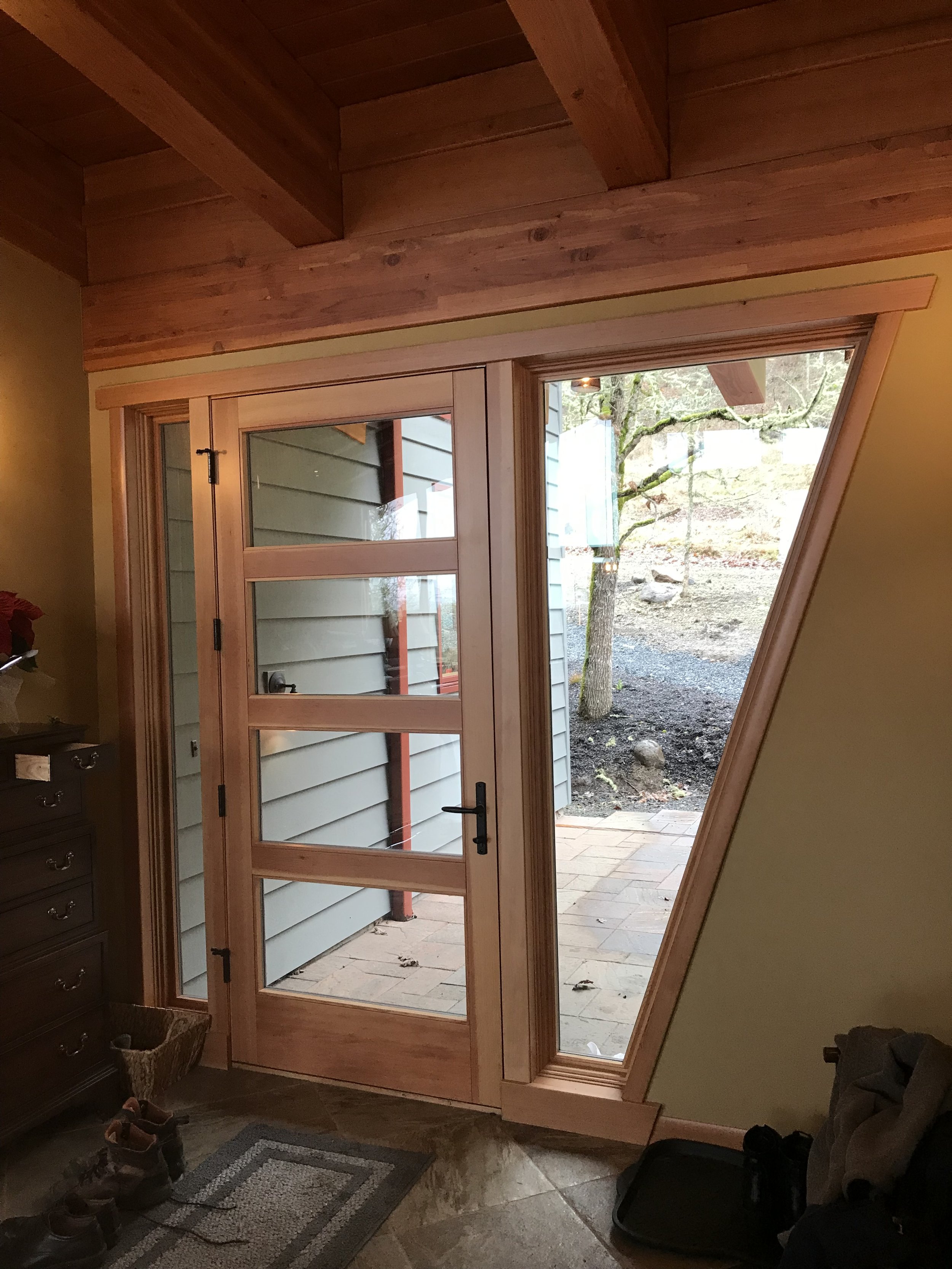 Ark Built Carpentry custom designed Inside view of a house door open to a backyard, showing a custom handcrafted wooden door with multiple glass panes, a stone pathway outside, and trees in the background.