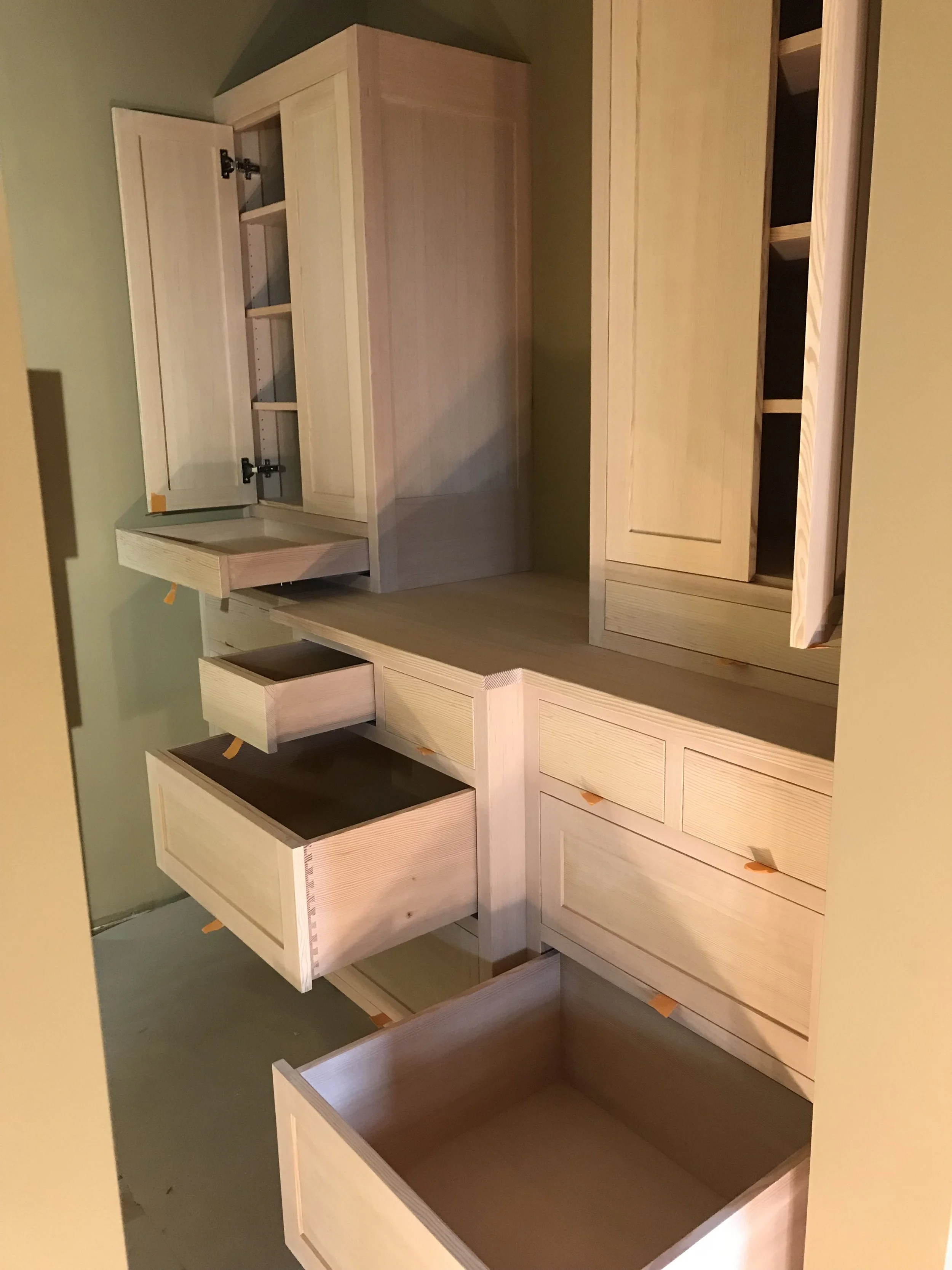Ark Built Carpentry custom designed handcrafted wooden closet with multiple drawers and open compartments set against a green wall.
