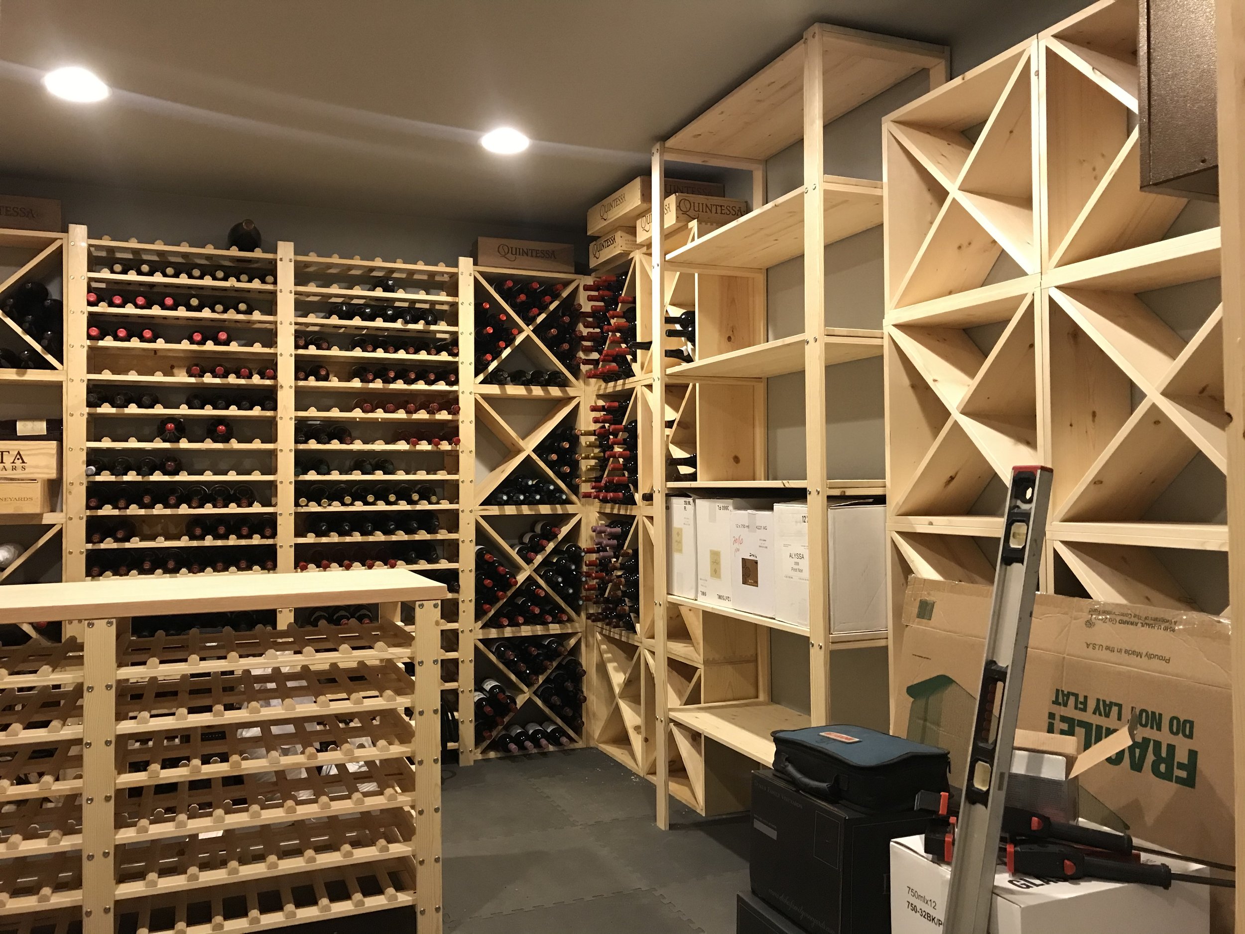 Ark Built Carpentry custom designed wooden wine racks filled with wine bottles, some empty shelves,  a step ladder, and a toolbox in a custom built wine cellar.