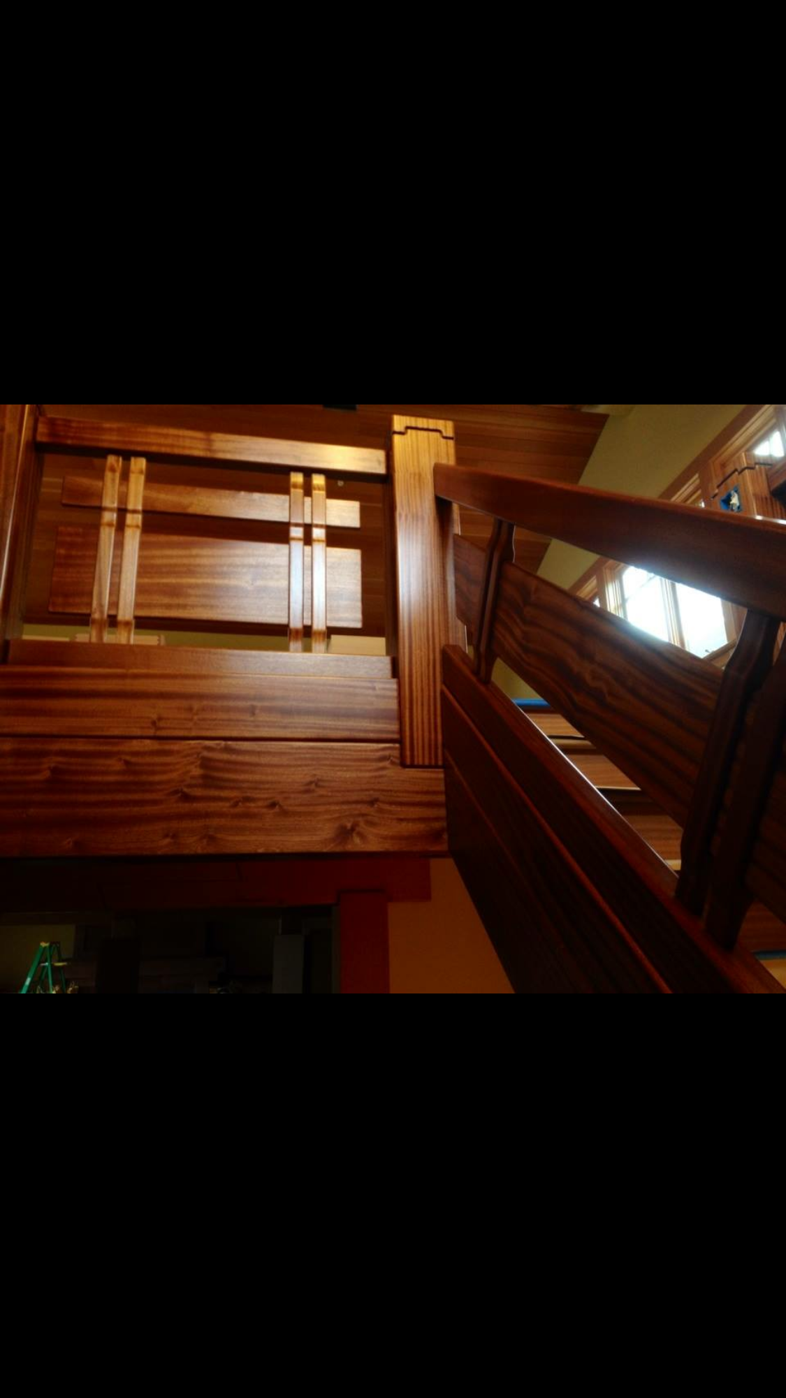 Ark Built Carpentry custom designed interior view of a wooden staircase with a handrail and steps leading to a second floor, natural light coming through nearby windows.