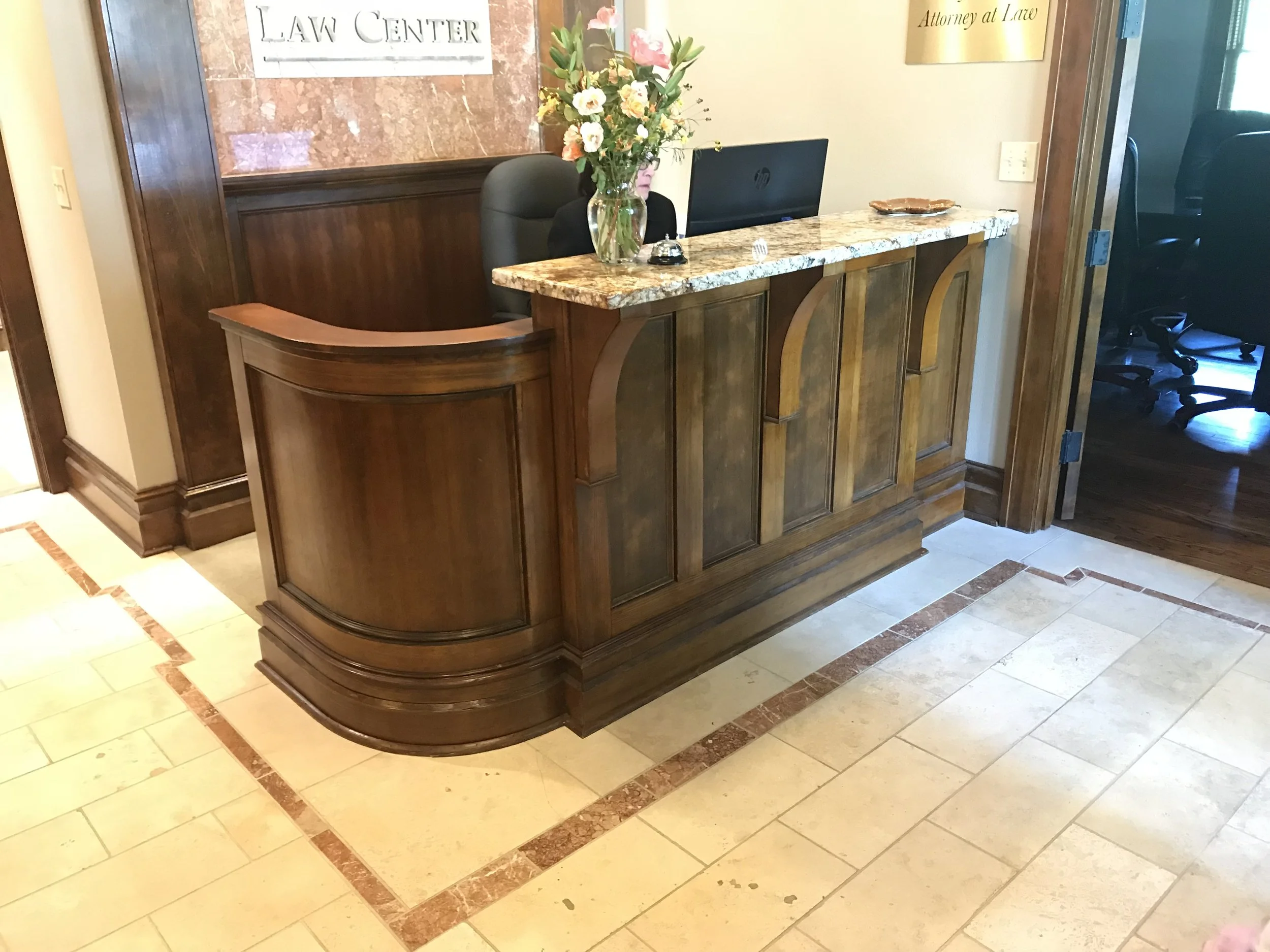 Ark Built Carpentry custom designed reception desk with a large floral arrangement in a glass vase, a computer monitor, a bell, and a decorative dish. Signs on the wall say "LAW CENTER" and "Attorney at Law." 