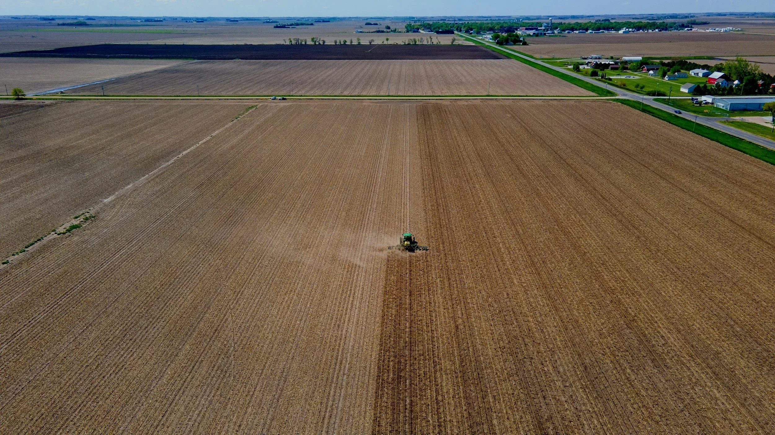 A green tractor working in a large, open farmland field during daytime.