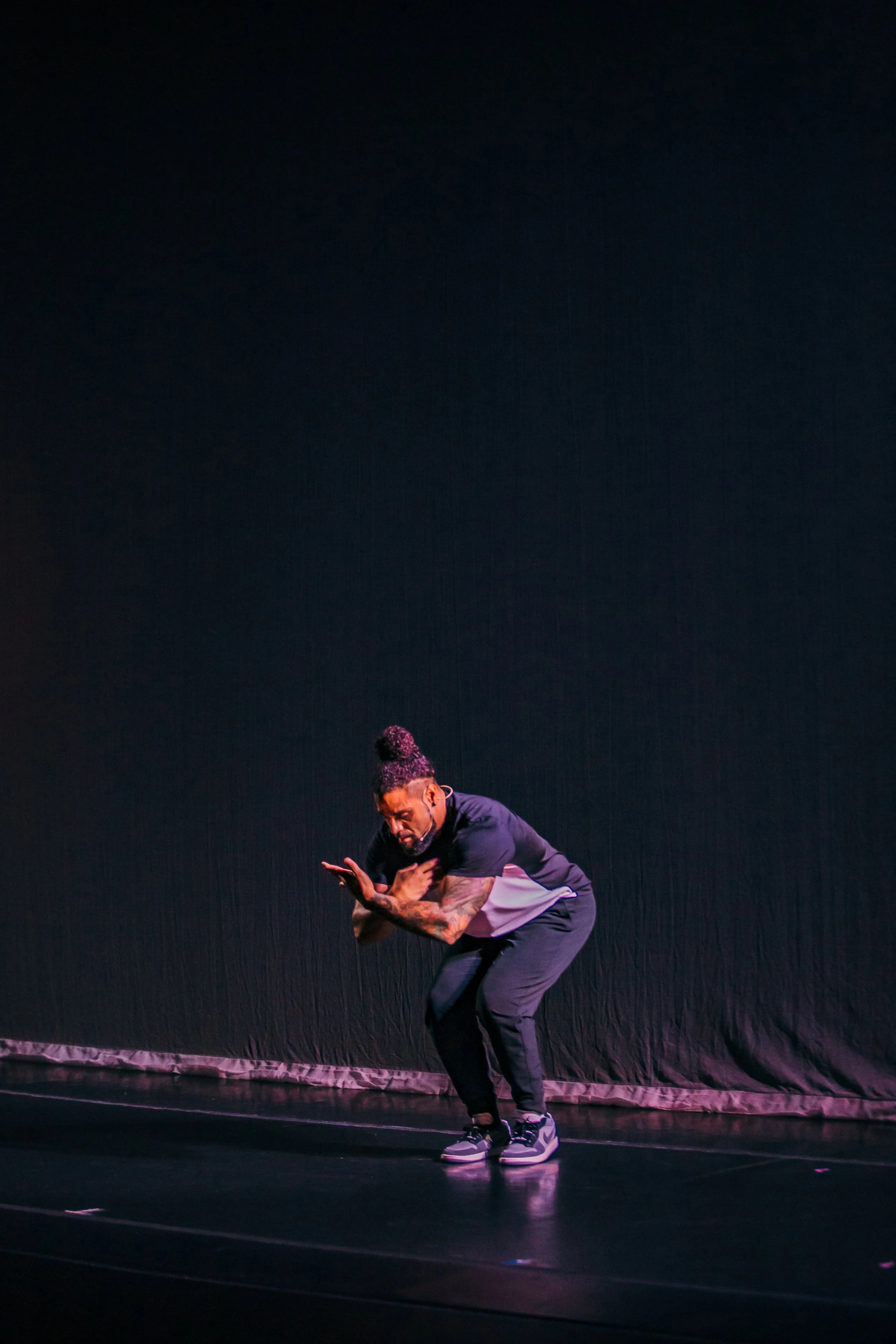 L.D. dancing moves on a dark stage, wearing black athletic clothing and sneakers, with his arms crossed over his chest and a focused expression.