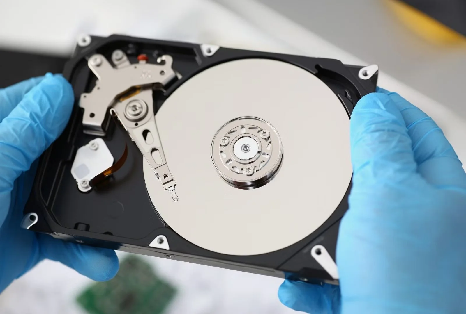 Person wearing blue gloves holding an open hard disk drive (HDD) with visible platters and actuator arm.