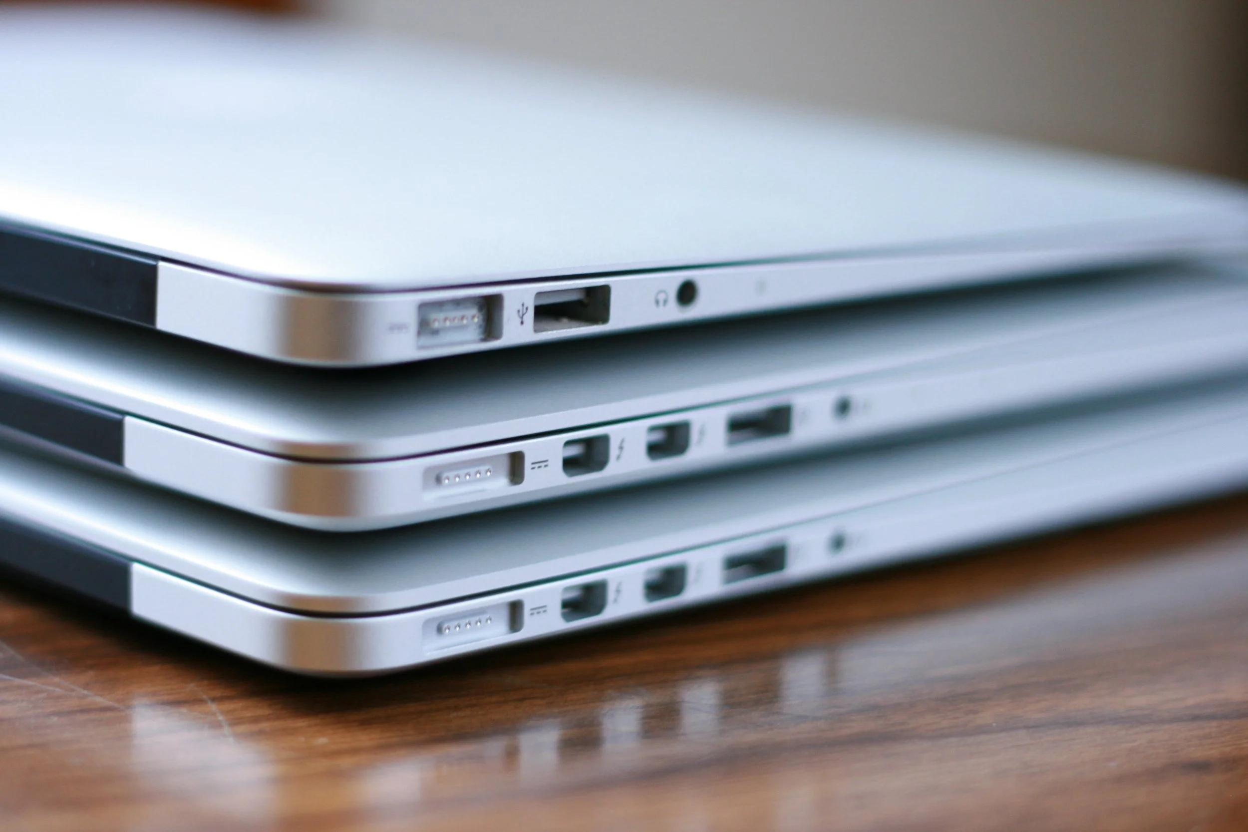 Stacked silver laptops with various ports on a wooden surface.
