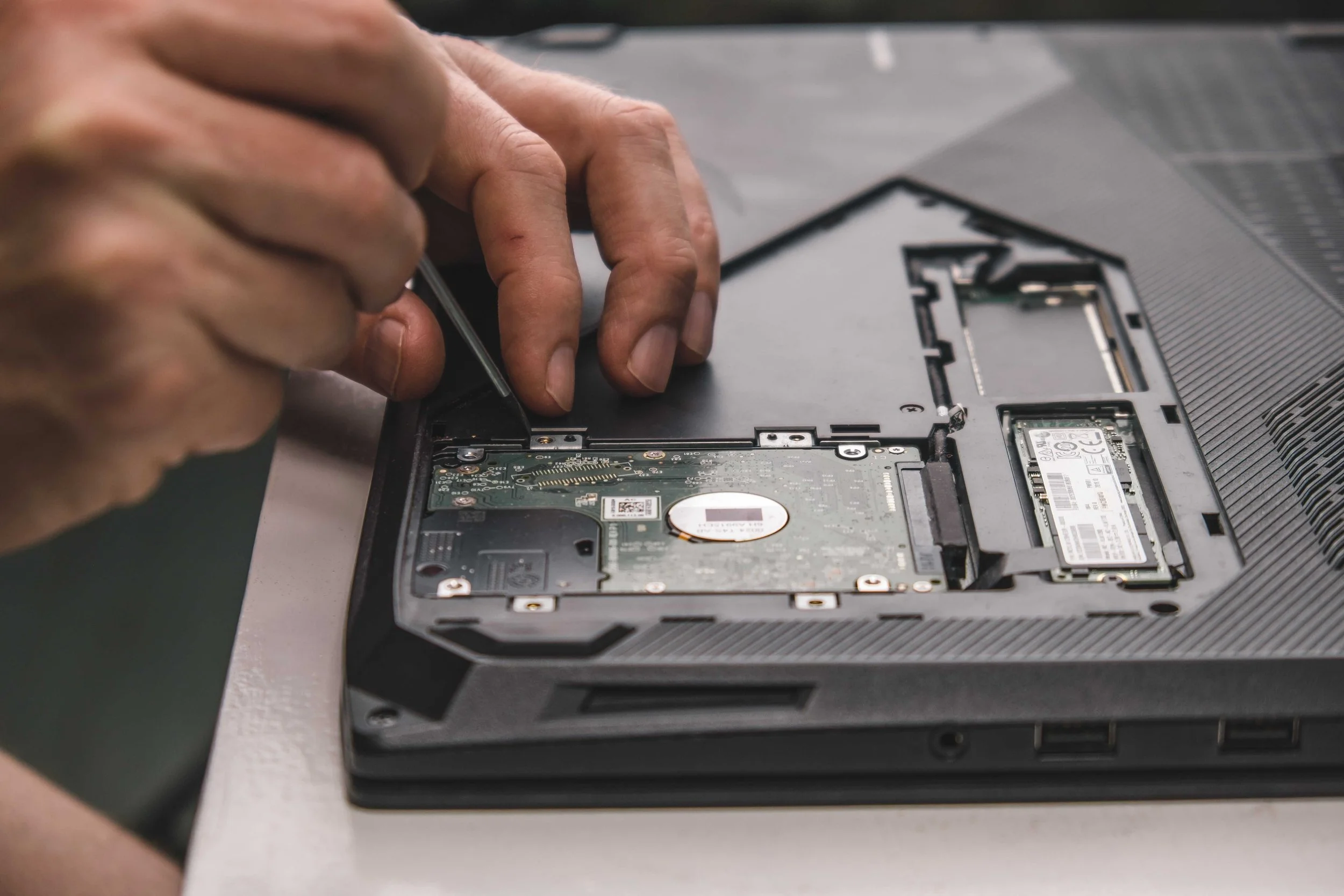 Person repairing a laptop, removing or replacing the hard drive with a screwdriver.