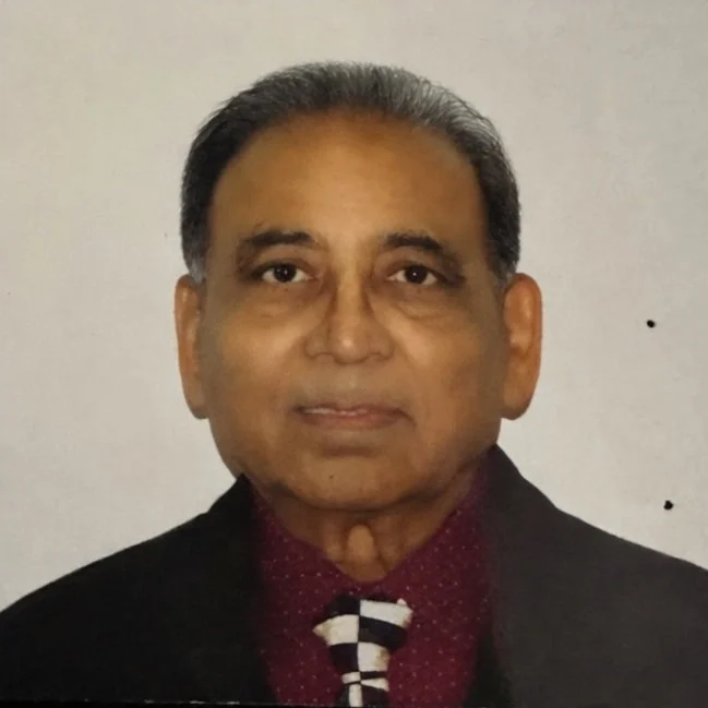 A portrait of a middle-aged man with dark hair and a serious expression, wearing a dark suit, red shirt, and a black-and-white checkered tie, standing against a plain background.