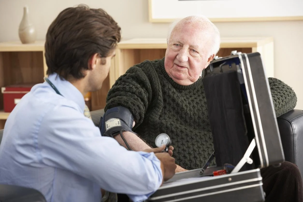 A healthcare professional checking a senior man's blood pressure during a medical exam in a well-lit clinic room.