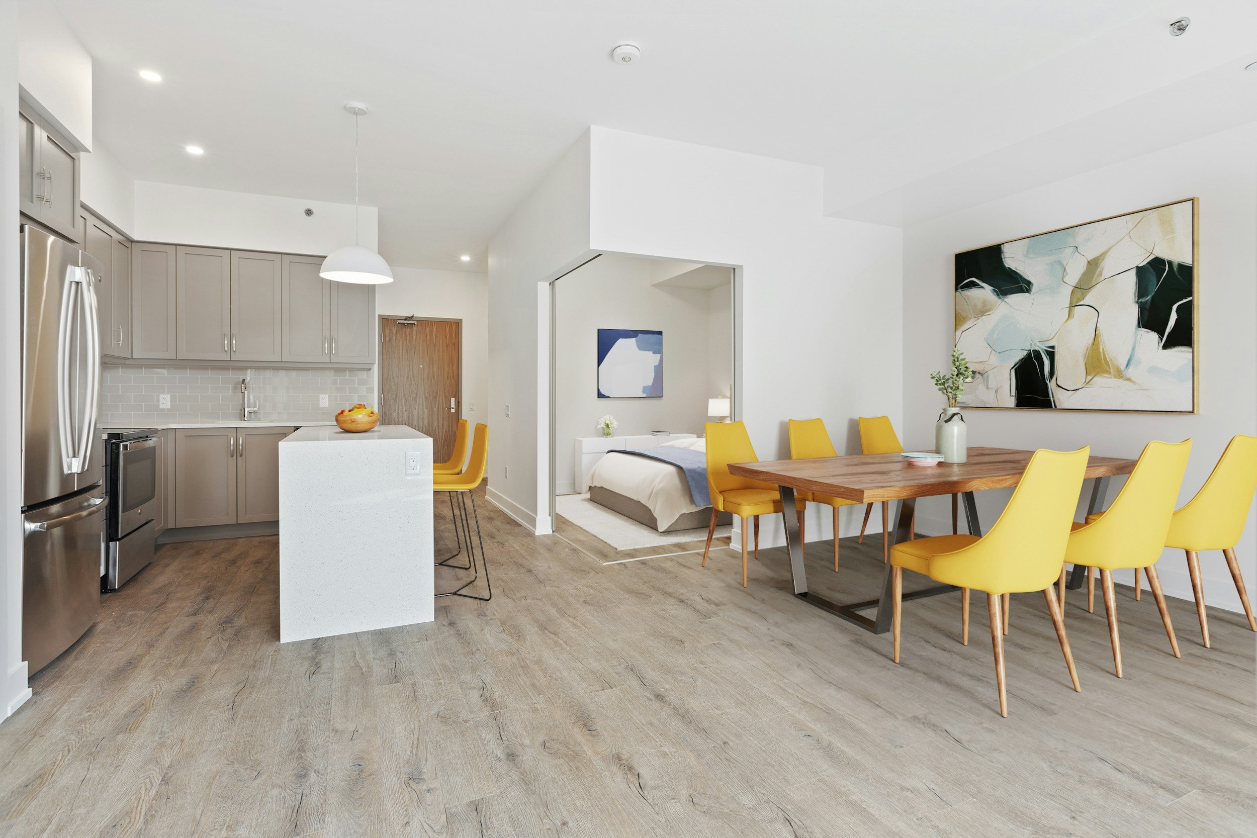 Interior de una vivienda moderna con cocina, comedor y un área de descanso, decorada con arte abstracto y muebles en colores amarillo y madera.