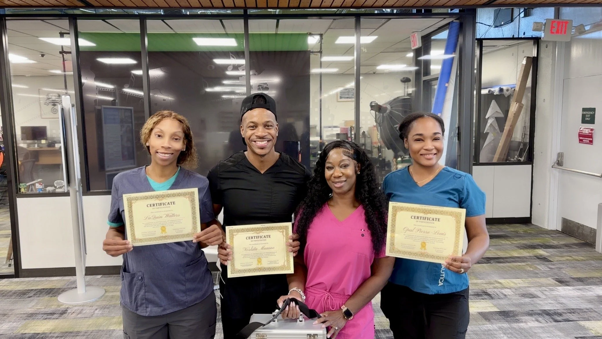 Four healthcare workers standing together in a clinic, holding certificates of achievement, smiling at the camera.