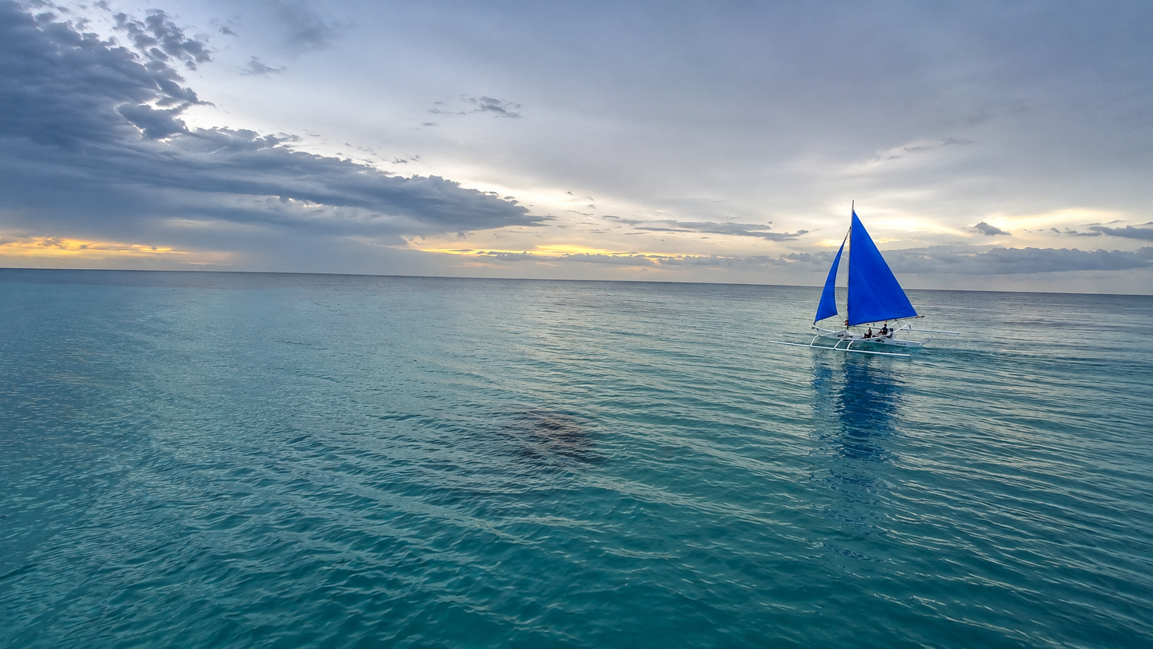 Traditional Philippine banca with a blue sail on calm tropical waters at sunrise, reflecting the island adventures that inspire Piggery Adventure Tales.