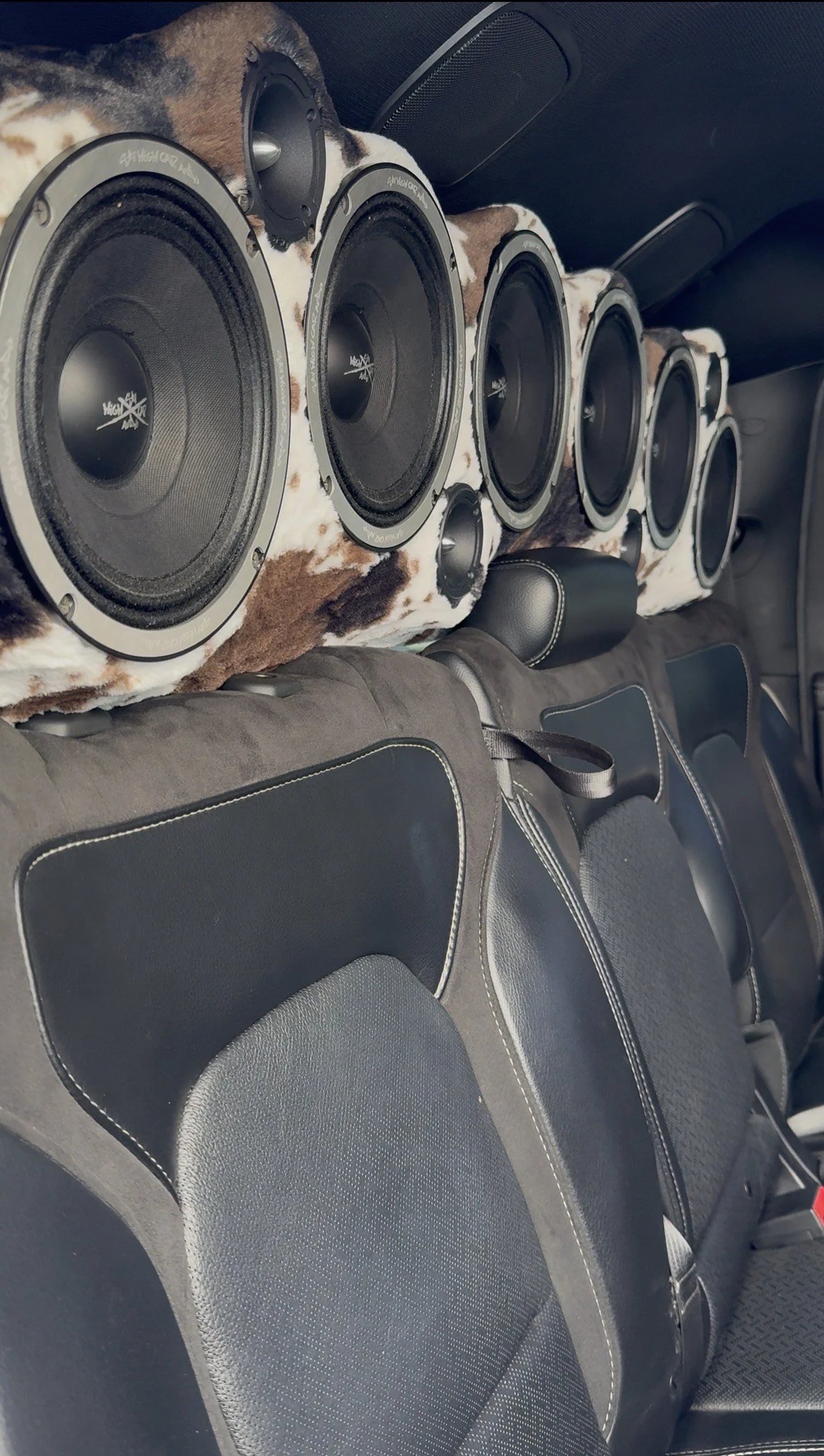 Car interior with large speakers and black leather seats with white stitching.