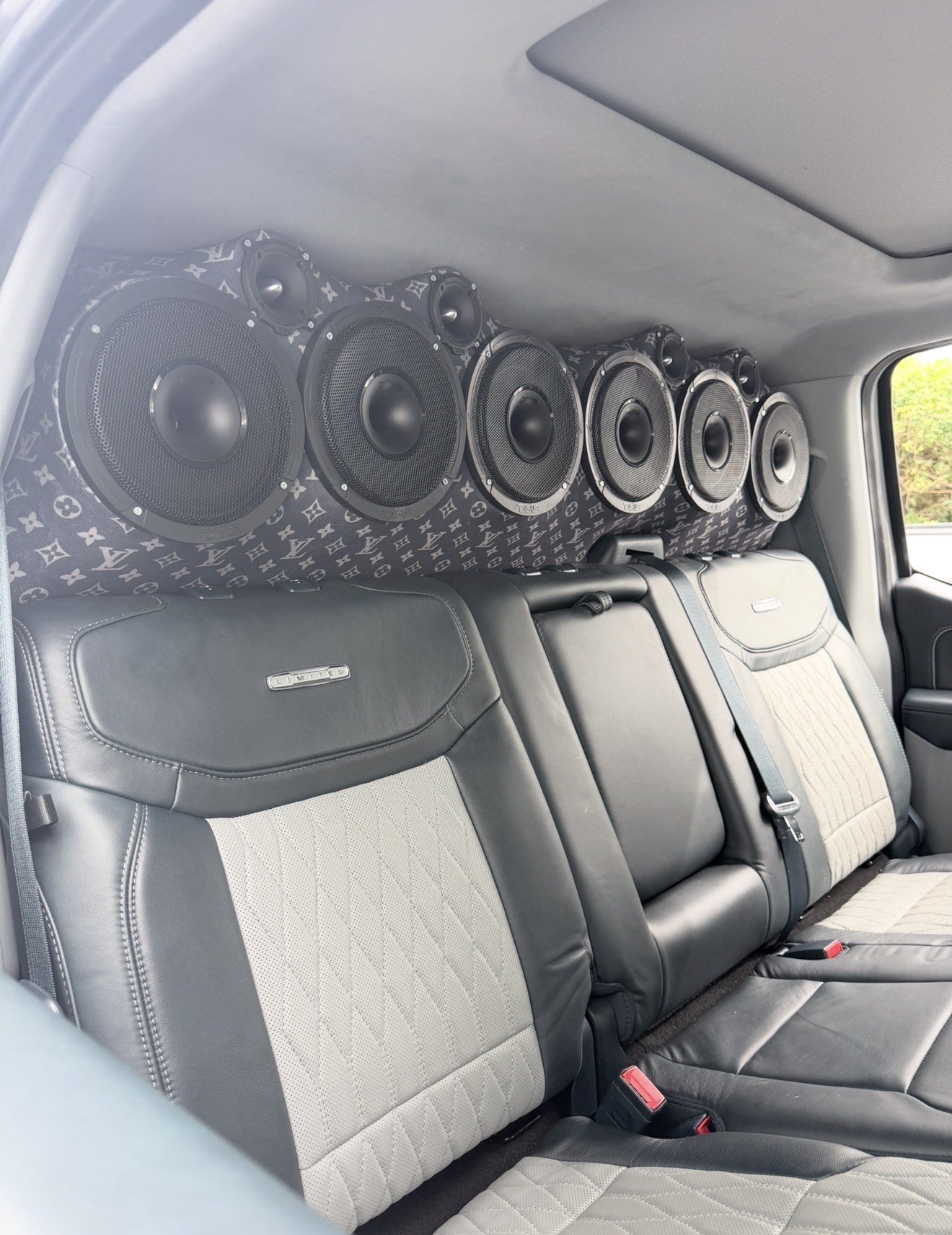 Inside a vehicle, there are large speakers installed along the back wall, with the interior featuring black and gray seats.
