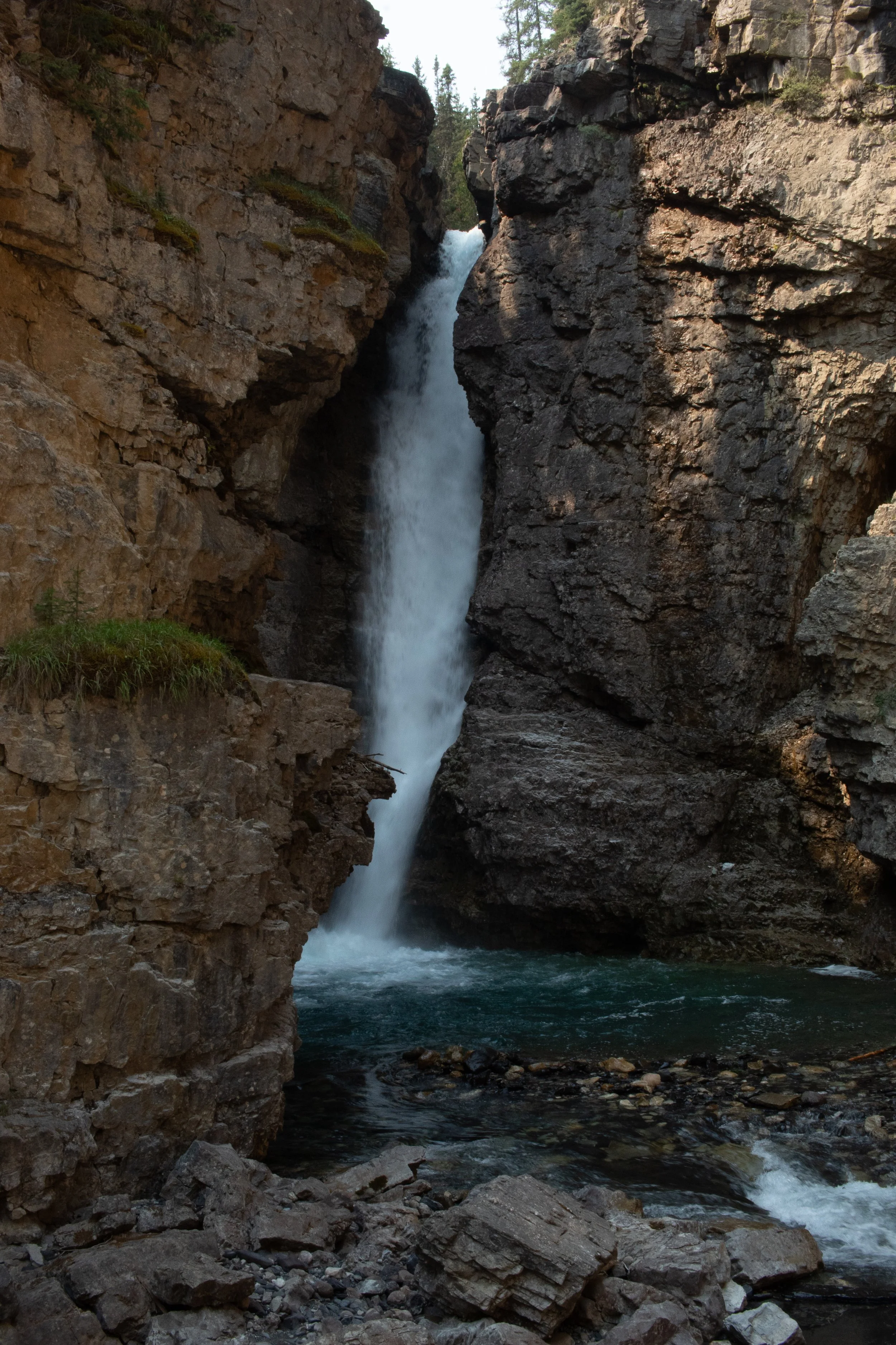 A waterfall flowing between rocky cliffs in a forested area.