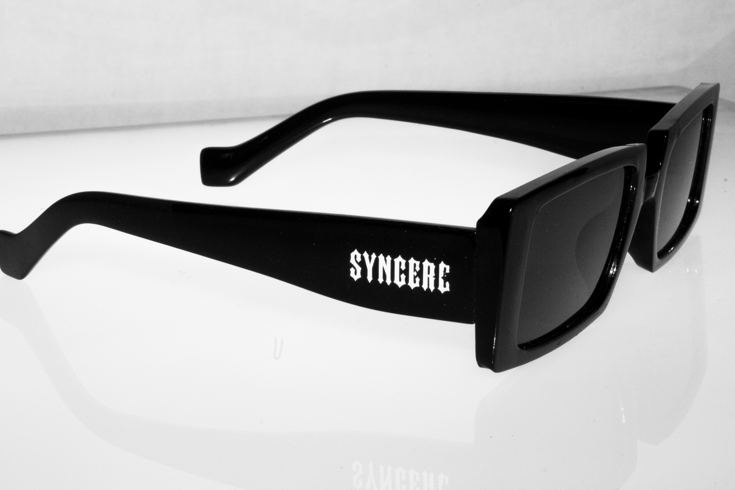 Close-up of black and white sunglasses with the word 'SYNGERe' printed on the side.
