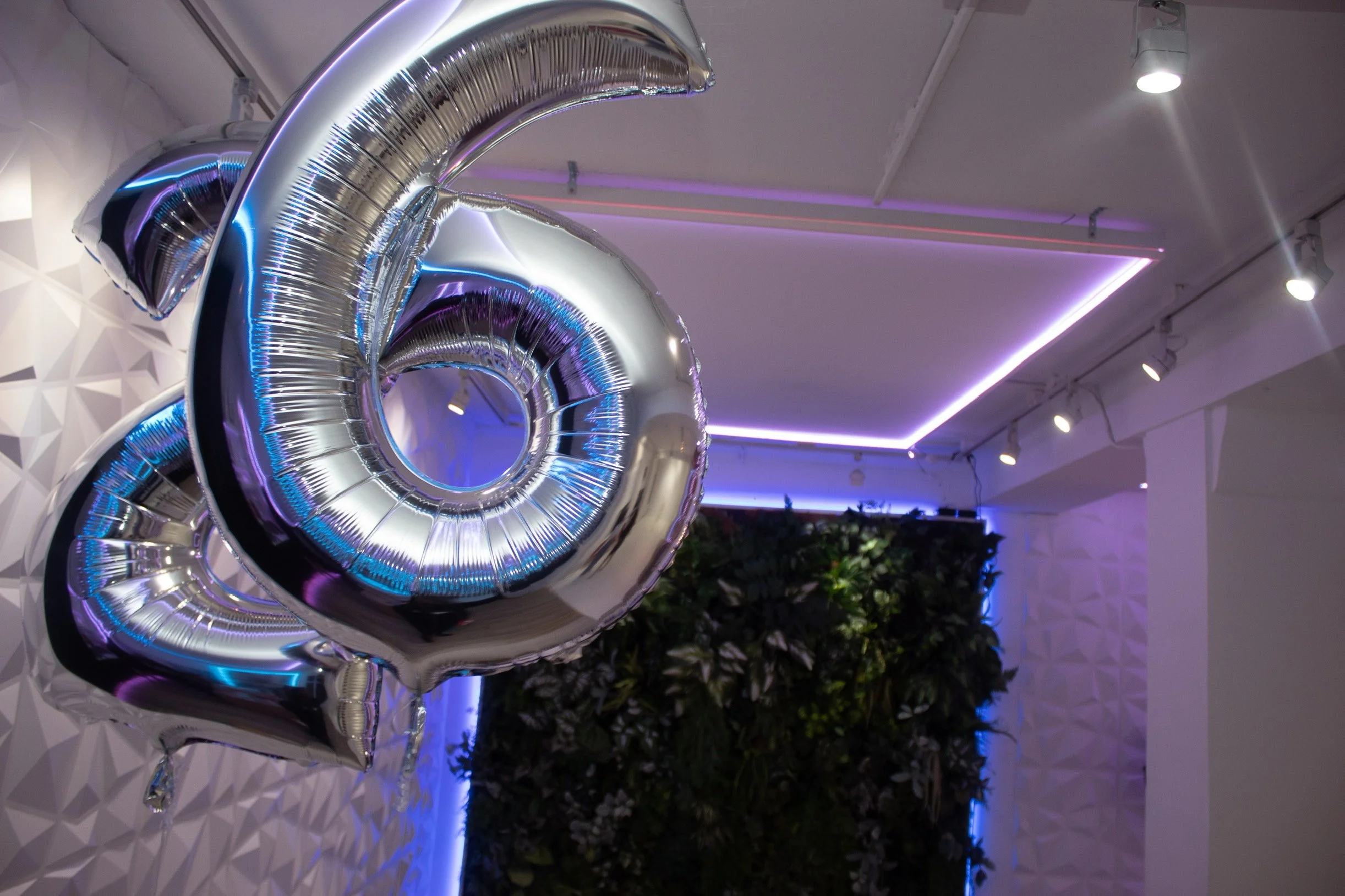 Silver balloon shaped as the number 0 in a decorated indoor space with purple and white lights and a textured white wall.