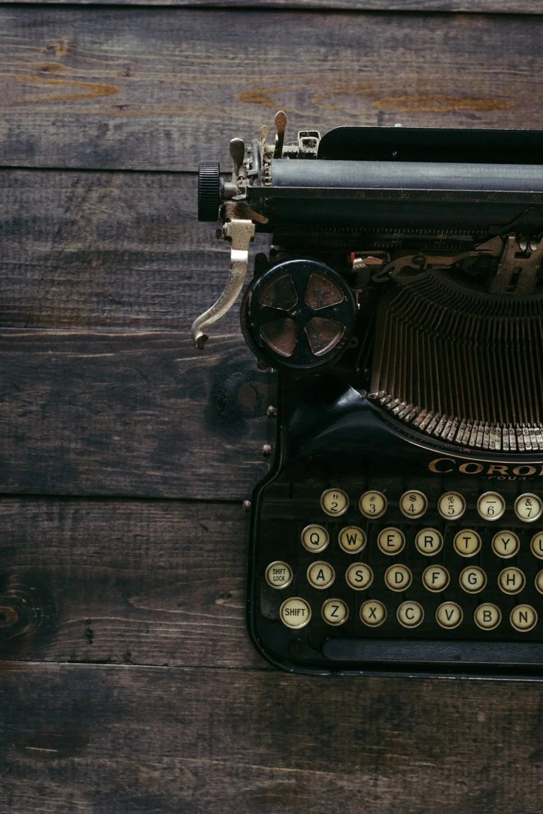 Top view of an old black typewriter with beige keys on a dark wooden surface.