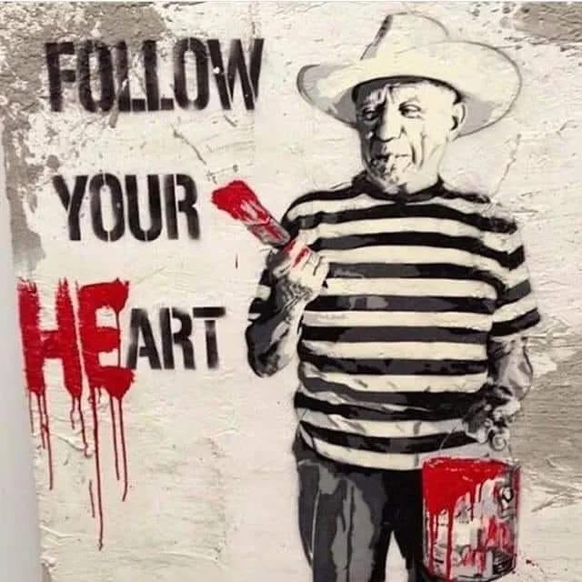 Street art mural showing a man in a striped shirt and a wide-brimmed hat holding a red paintbrush and a paint bucket, with the phrase "Follow Your Heart" next to him. He has painted "HE" in front of the word "ART' to spell "Heart".