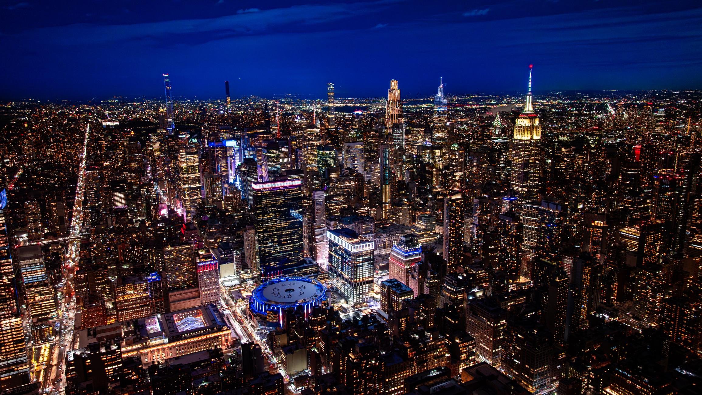 Nighttime aerial view of New York City skyline with illuminated skyscrapers and streets.