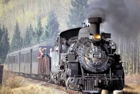 A black steam locomotive train pulling passenger cars through a forested area, with a vintage style and smoke coming from the chimney.