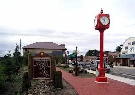 Red clock tower on a sidewalk with a building and street in the background