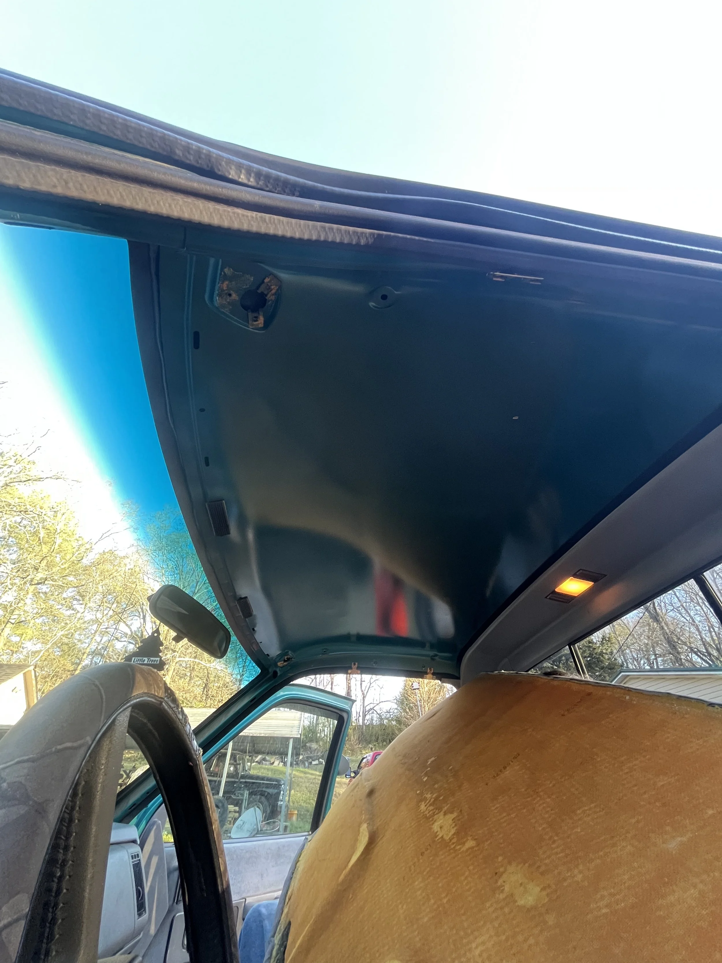 The interior of a vehicle with the hood raised, showing the inside of the roof and a yellow cushion or object on the passenger seat.