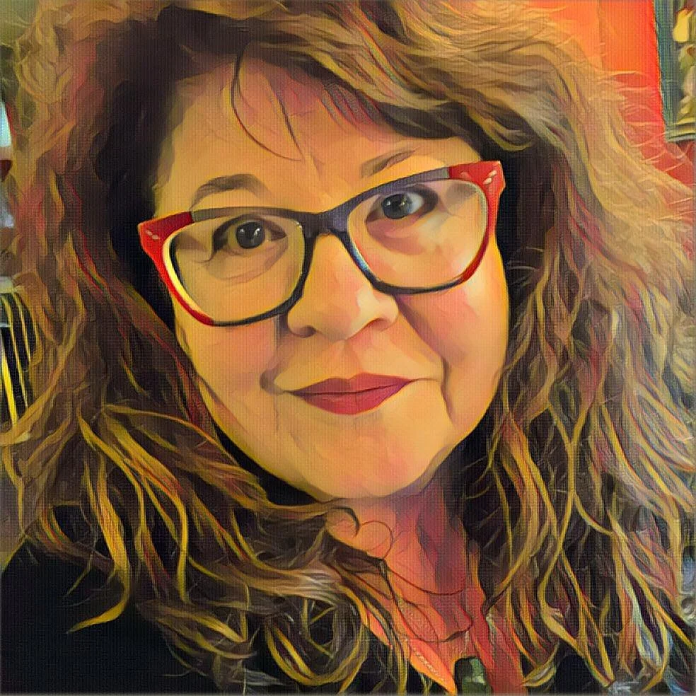 A woman with curly hair wearing red and black glasses, smiling at the camera.