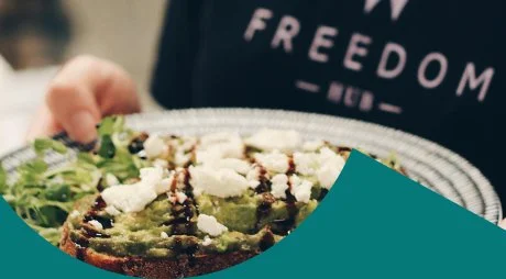 A plate of gourmet food being served, with a Freedom Hub apron visible in the background.