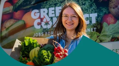 A woman smiling at a Green Connect market stall, surrounded by fresh vegetables and fruit, with a 'Jobs for the Planet' banner behind her.