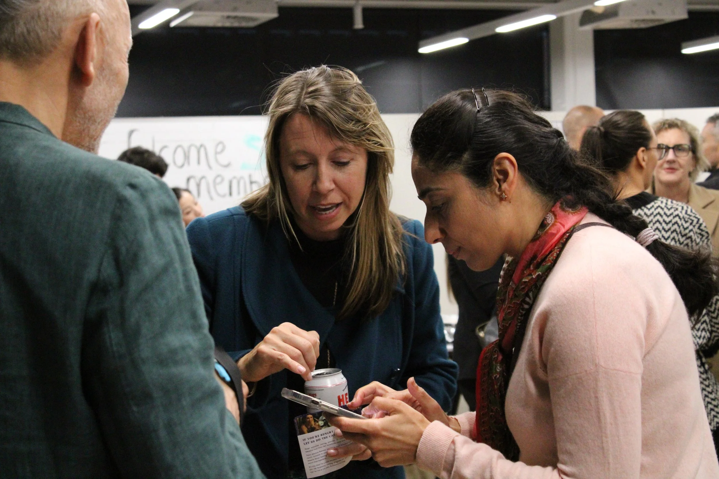Two women in close conversation at a networking event, one showing something on her phone.