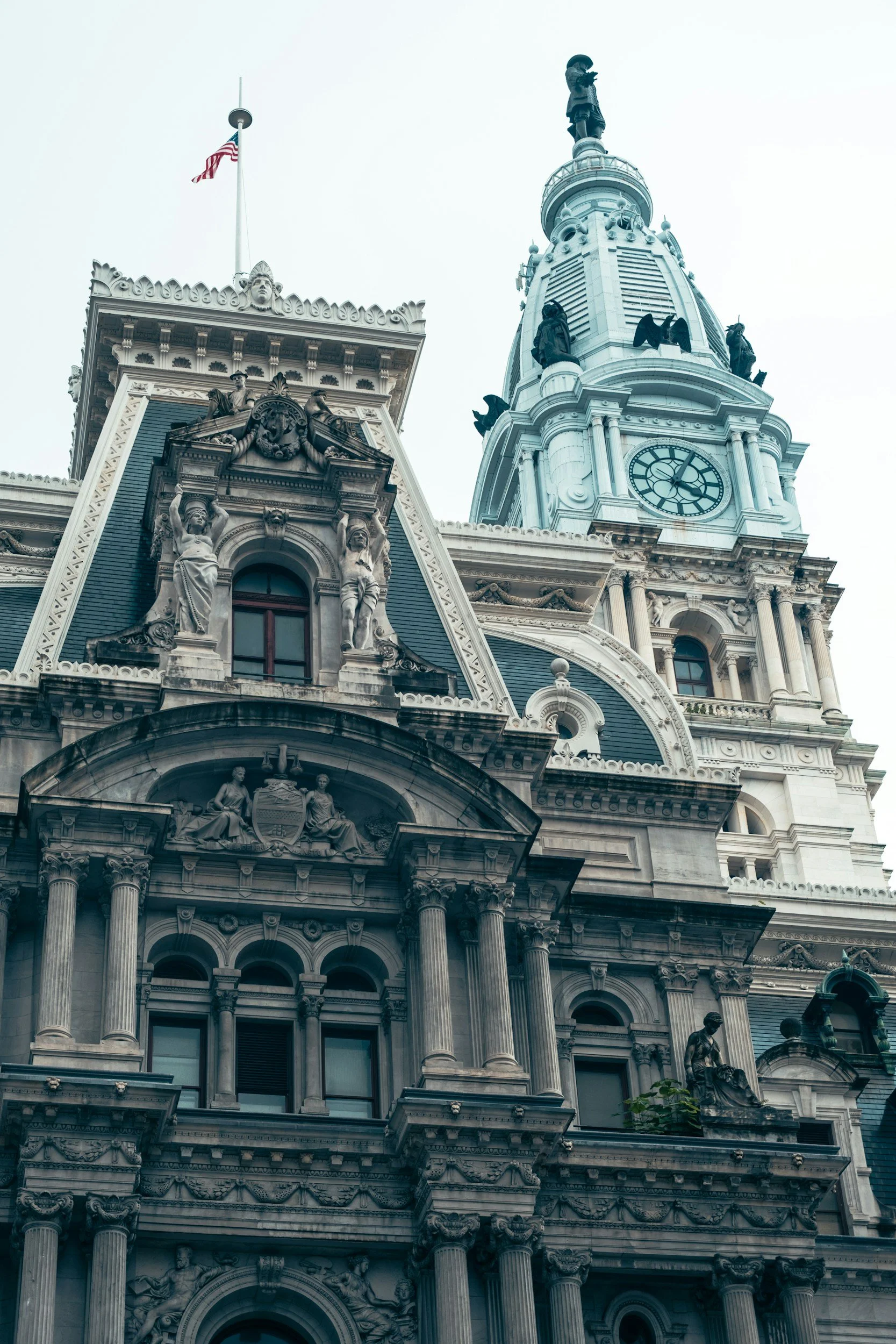 Low-angle view of a historic church or city hall with ornate architectural details, statues, columns, clock, and a flagpole with an American flag