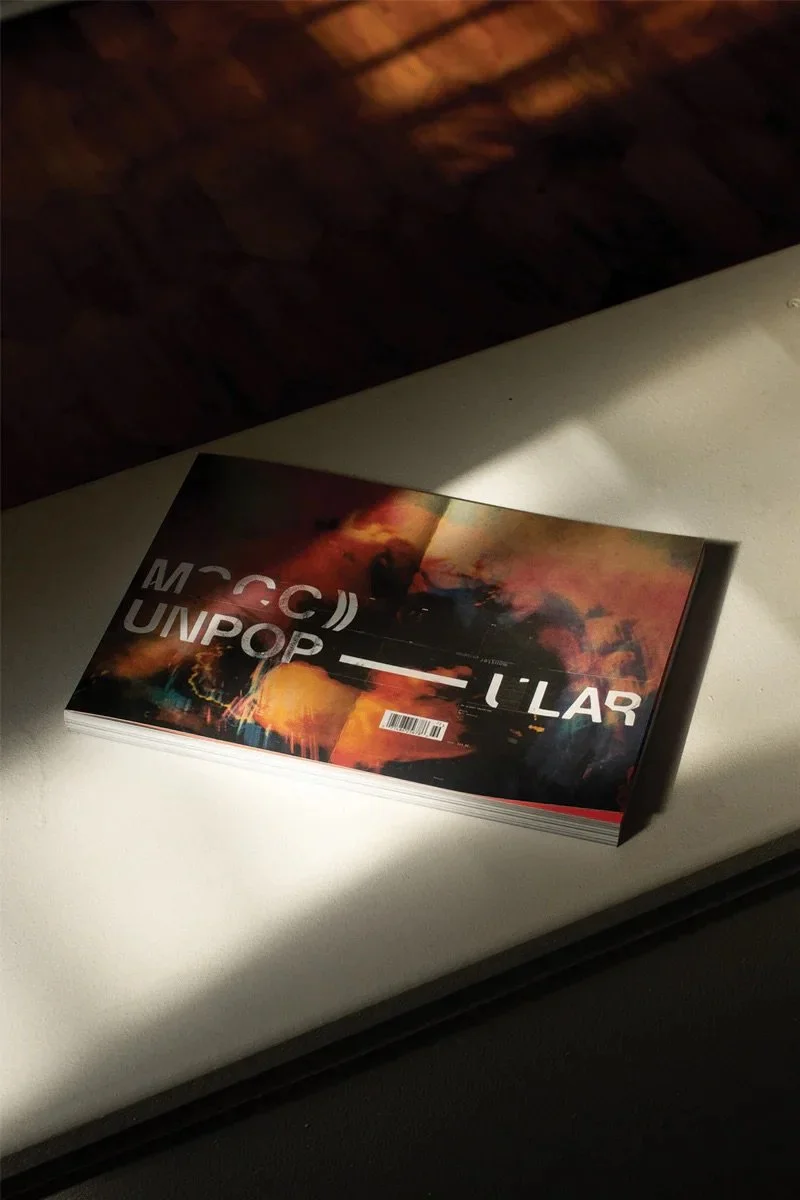 A thick book or magazine with a dark, fiery abstract cover design on a white surface, with a barcode at the bottom center.