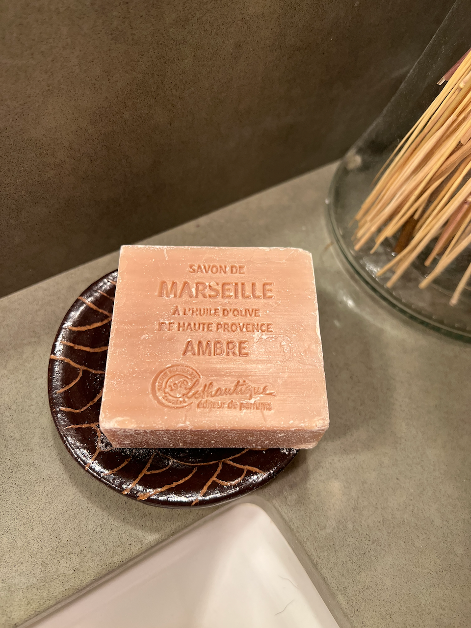 A bar of handmade soap with embossed French text resting on a decorative dish.
