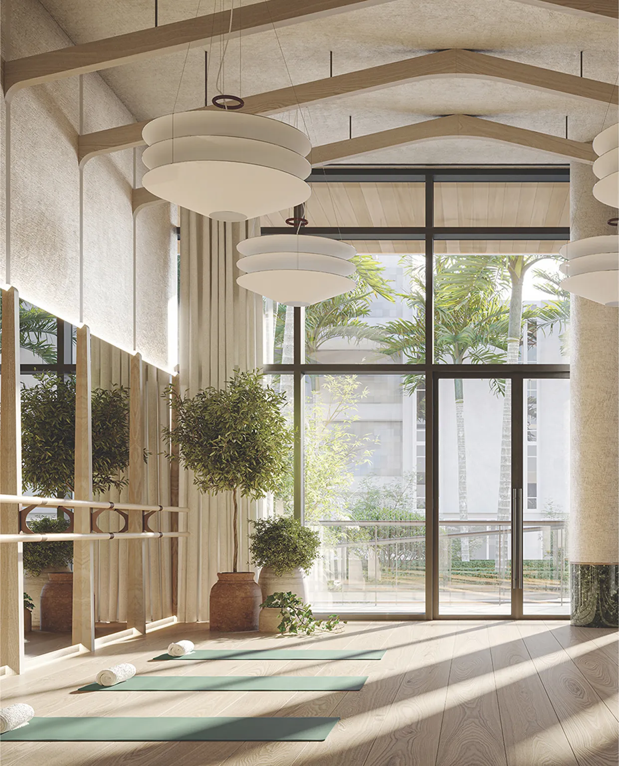 Bright indoor yoga studio with large windows, green mats, rolled towels, potted plants, hanging pendant lights, and wooden decor.