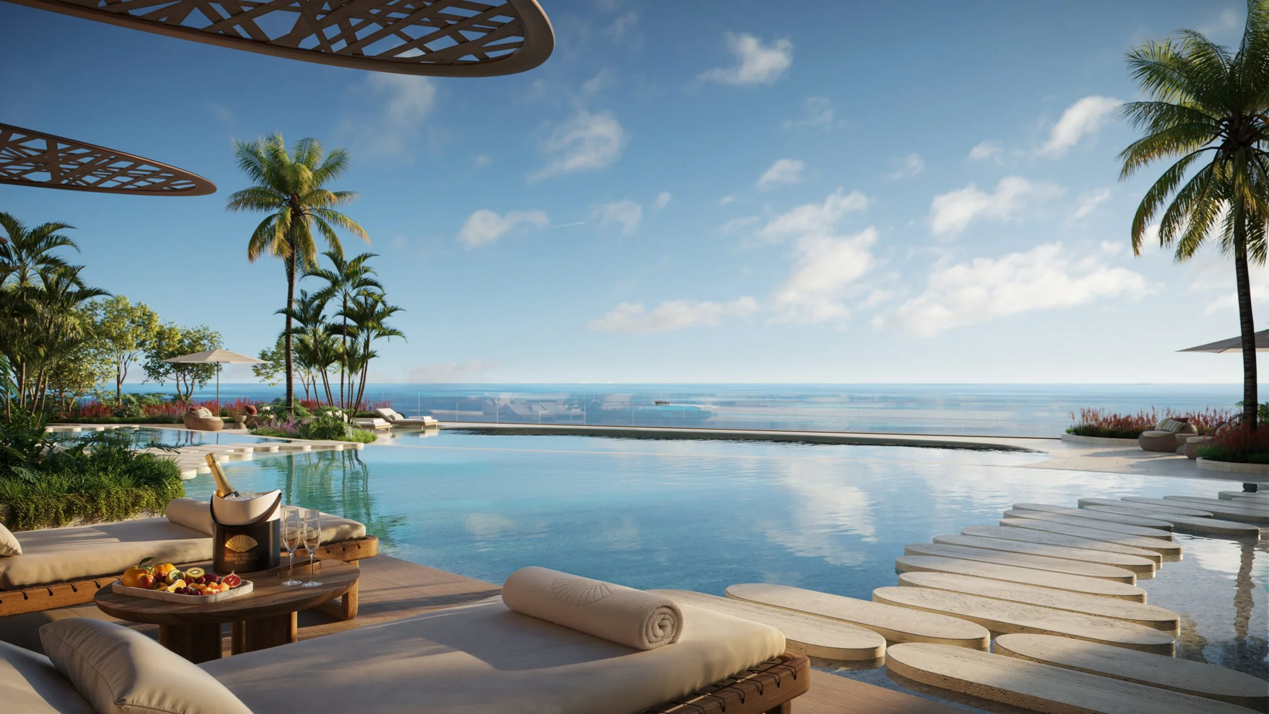 Luxury poolside lounge area with palm trees, lounge chairs, umbrellas, a scenic ocean view, and a mountain of fruit and champagne on a round table.