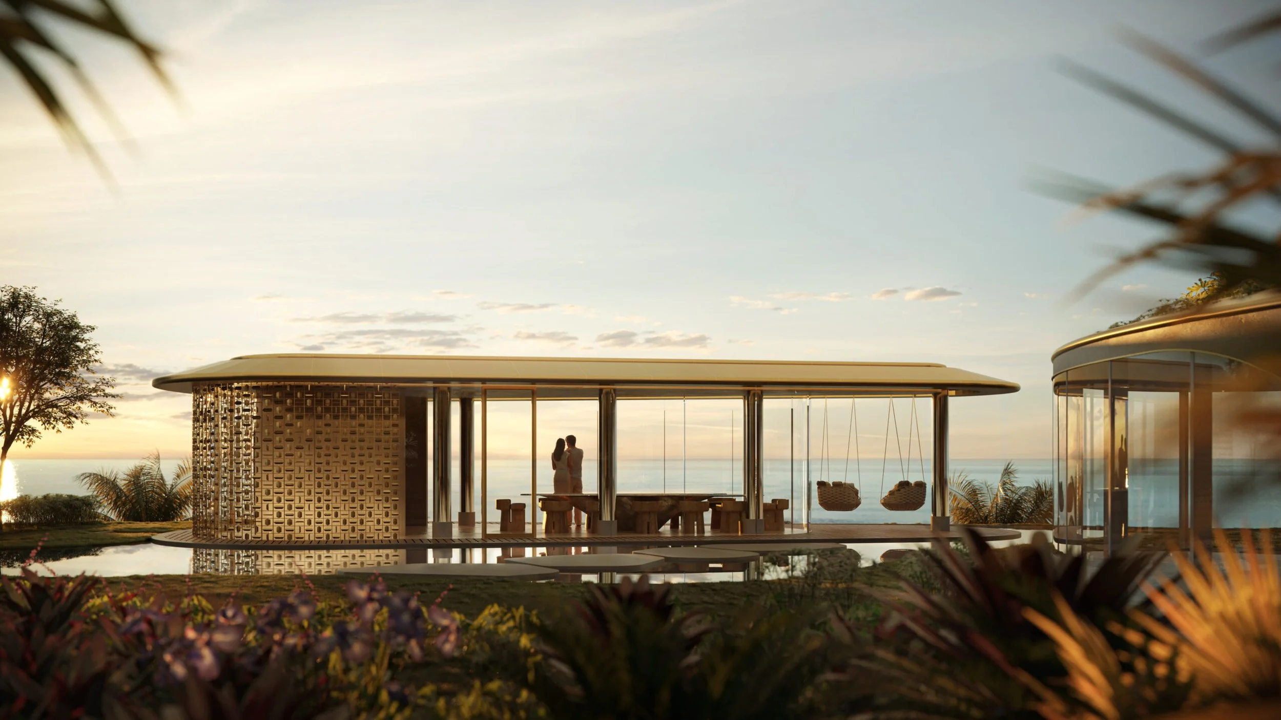 Modern house with large glass windows overlooking the ocean at sunset, with two people standing inside and two hanging chairs outside.