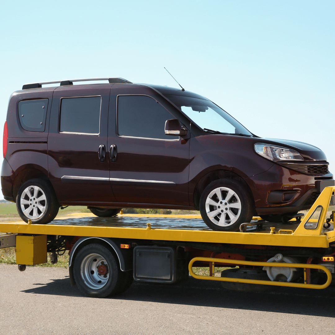 A dark red compact van on a yellow flatbed tow truck.