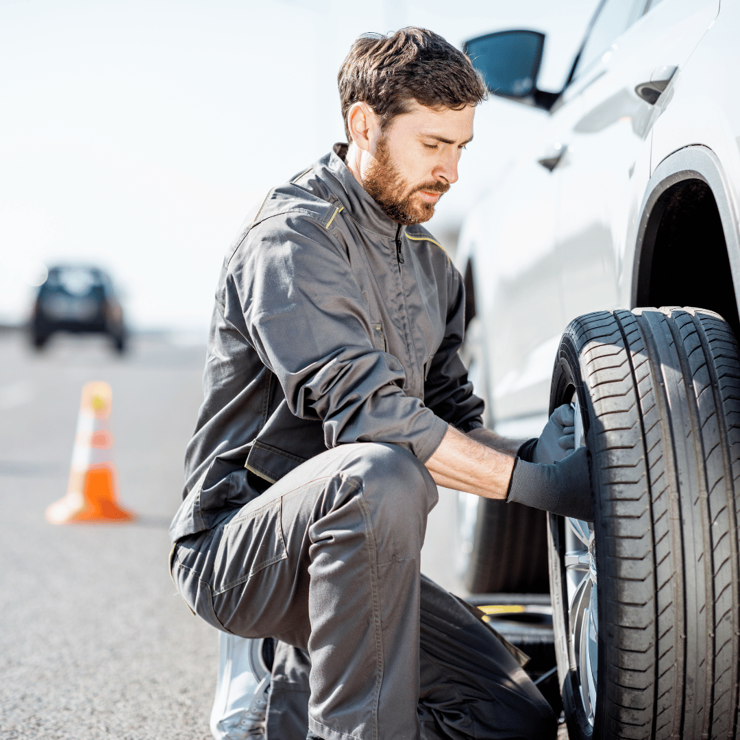 Man changing a flat tire on a white car on the highway