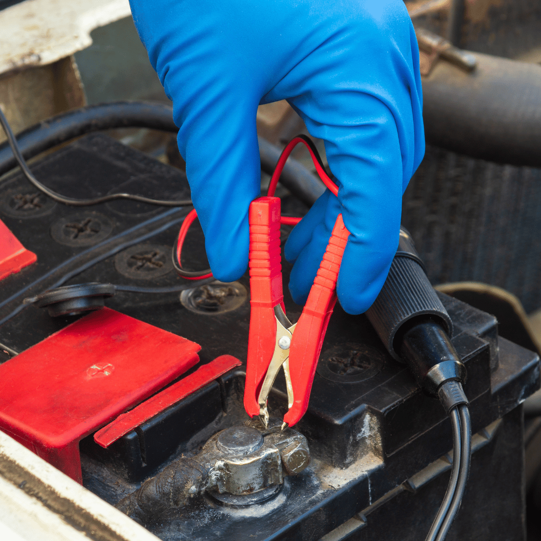 A person wearing a blue glove is using red alligator clips connected to a black car battery.