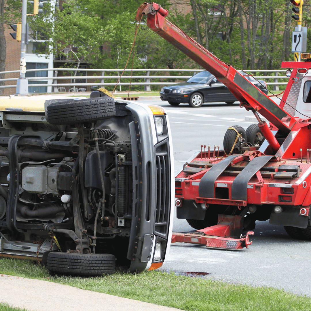 A vehicle has flipped onto its side after a collision, with a tow truck present at the scene.