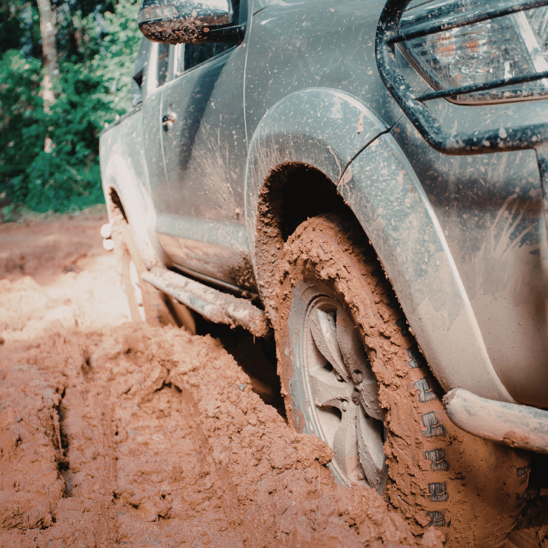 A muddy off-road vehicle stuck in dirt with mud covering the tires and side of the vehicle.