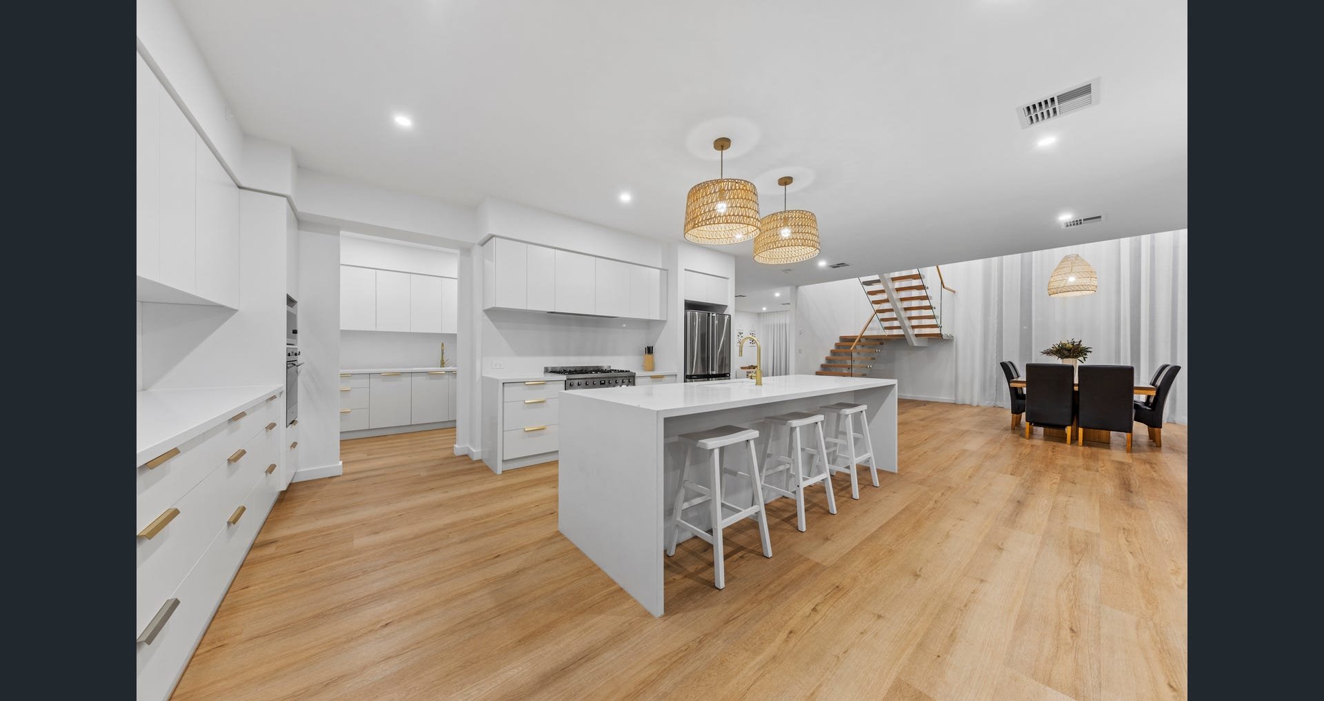 Modern white kitchen with an island, pendant lights, and a dining area with a round table and chairs in the background.