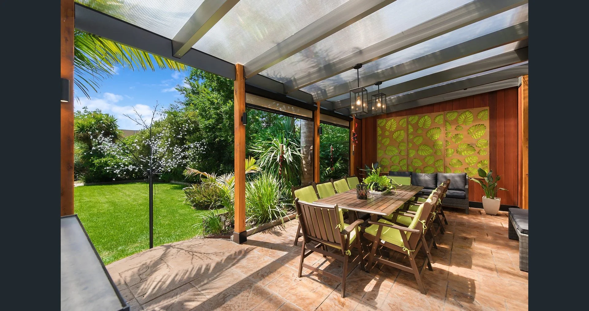 Outdoor patio with wooden dining table, chairs, and lush garden view under a transparent roof.