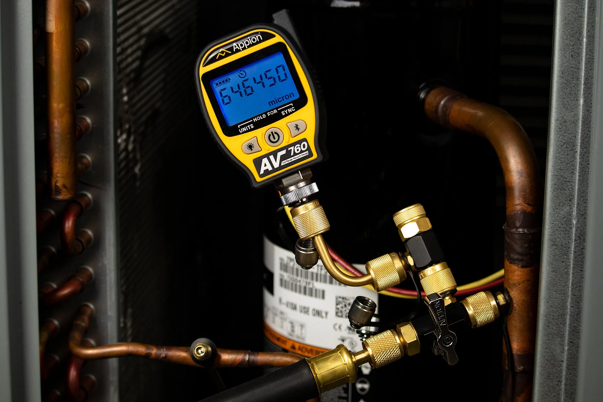 A digital multimeter connected to refrigeration or HVAC copper piping to measure pressure or temperature.