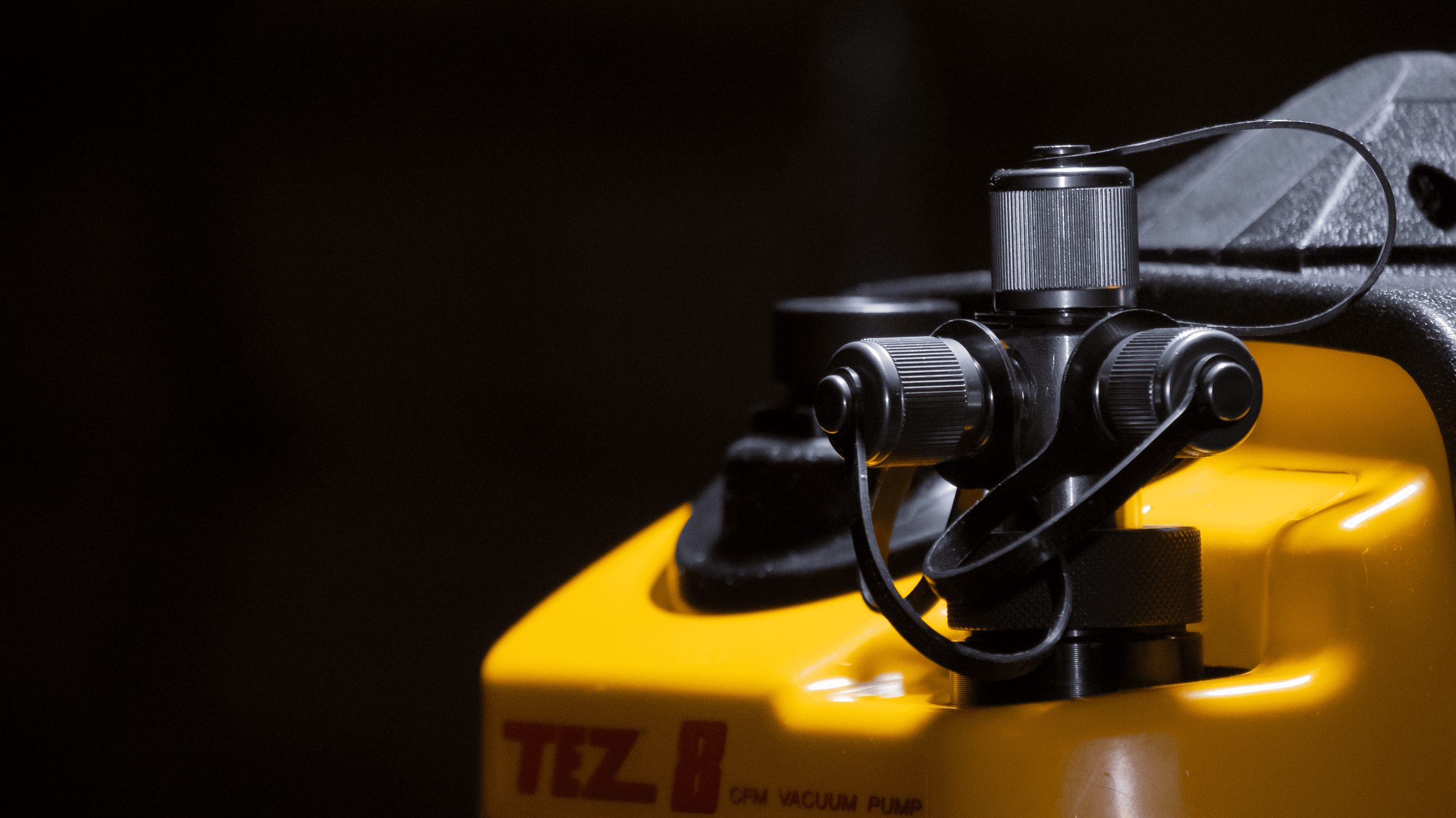 Close-up of a yellow TZX-8 CFV vacuum pump with black control knobs and hose connections, set against a dark background.