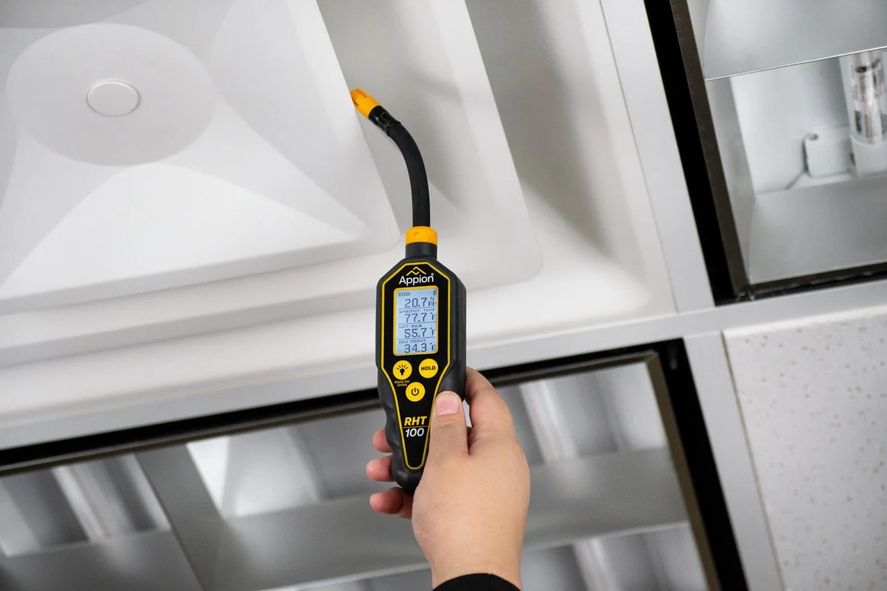 A person holding a digital thermometer measuring refrigerant temperature inside a commercial refrigerator or freezer. The display shows multiple temperature readings.