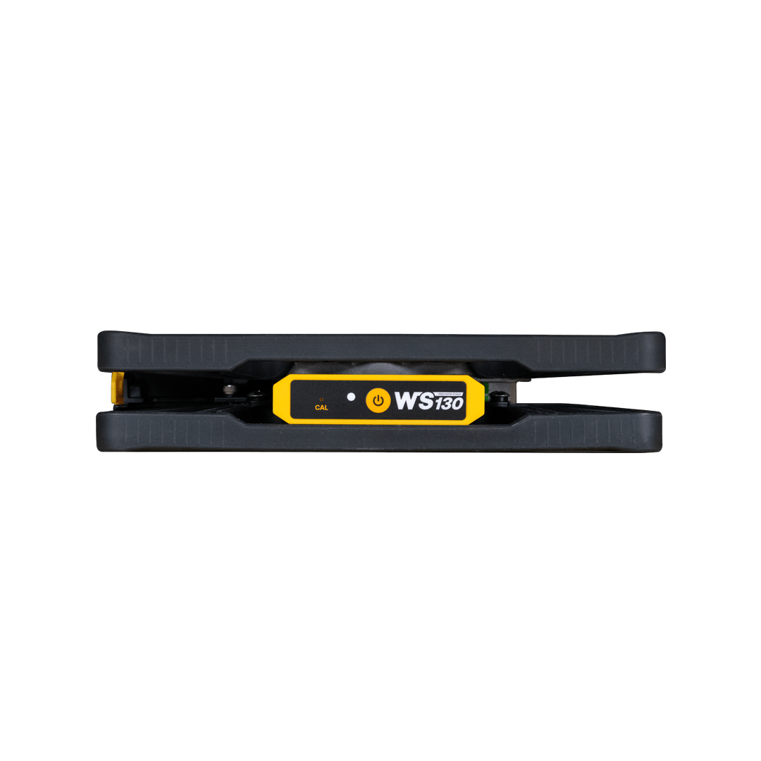 A black and yellow skateboard calibration and measurement device called WS130, placed between two black rubber mats against a black background.