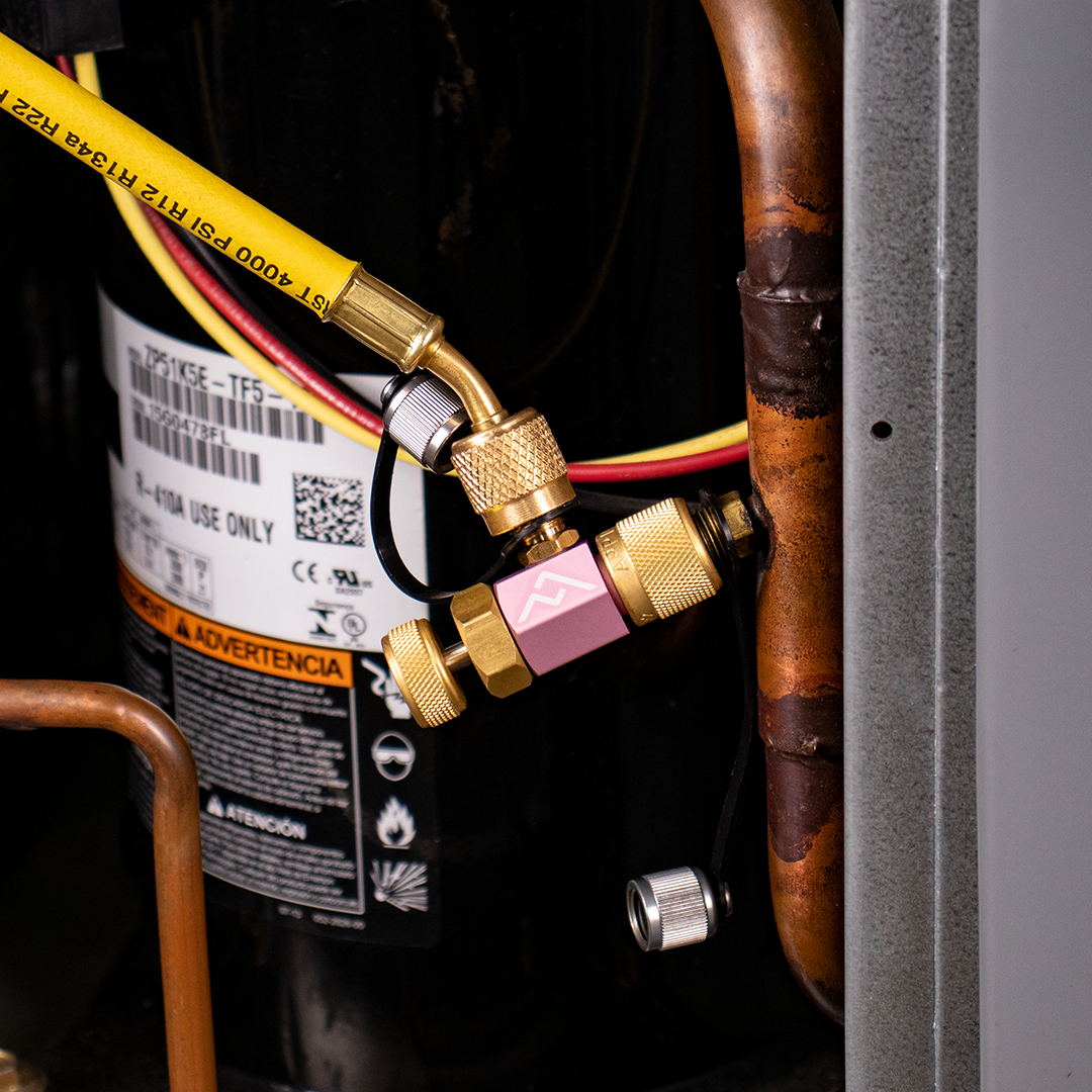Close-up of a refrigeration compressor with yellow, red, and black wires connected to brass fittings attached to copper and steel pipes.